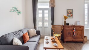 A living room with a grey sofa, a wooden coffee table with cups and pastries, a wicker chair, and a wooden cabinet with a decorative towel. - Coquillages et Crustacés - Apt avec balcon vue mer (Saint-Malo)