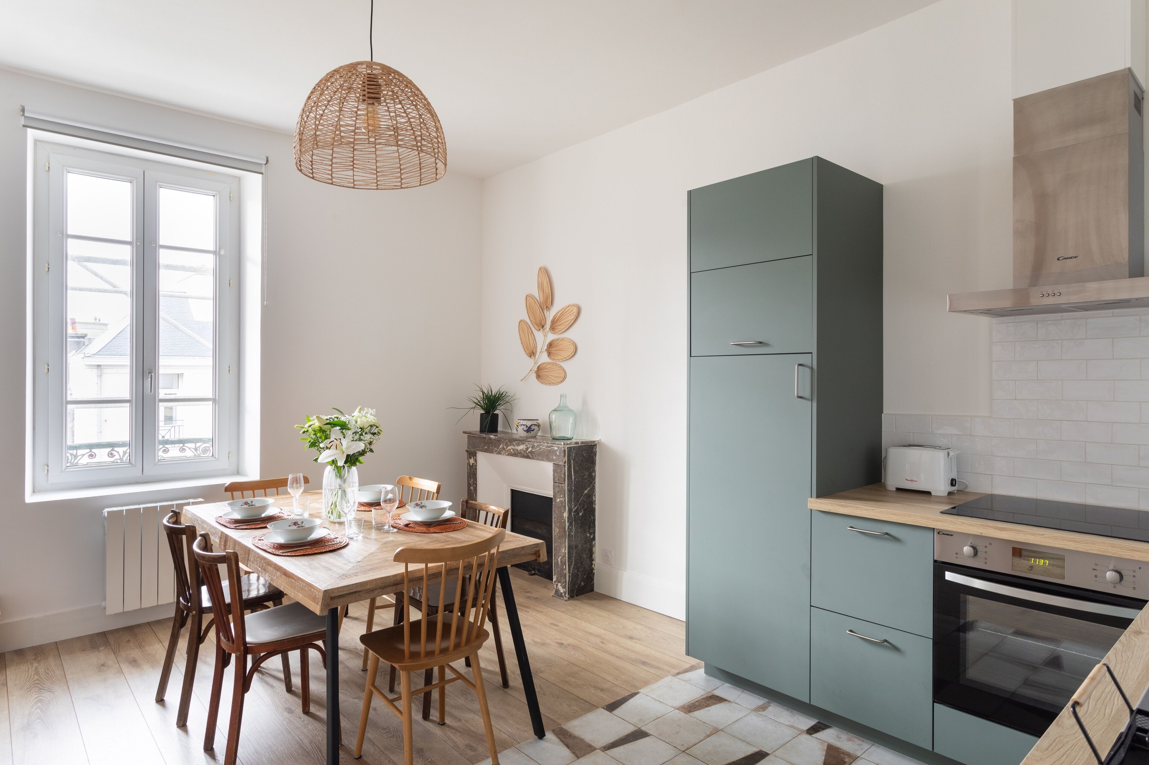 A modern kitchen with a dining table, chairs, a hanging light fixture, a built-in oven, and a green cabinet.