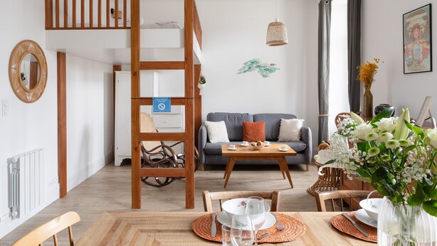 A modern living room with a loft bed, a sofa, a dining table set, and a large window with curtains. - Coquillages et Crustacés - Apt avec balcon vue mer (Saint-Malo)