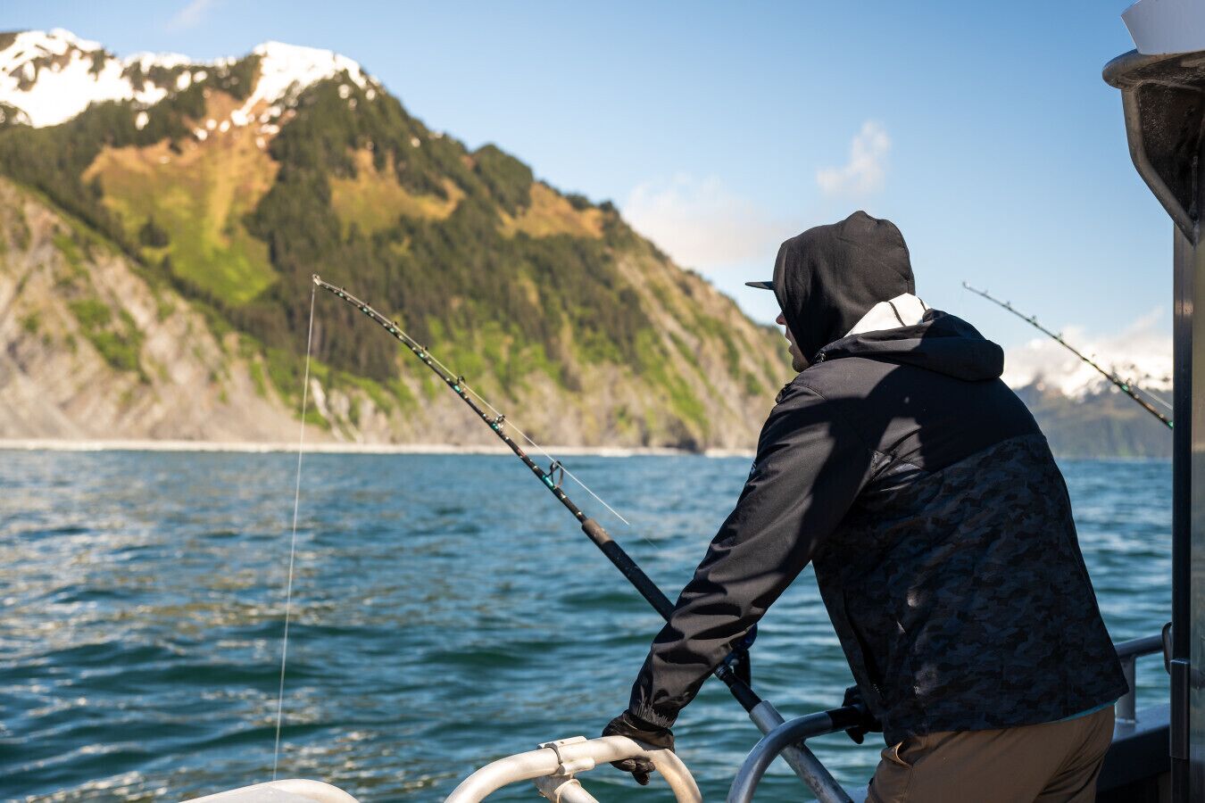 A person fishing on a boat with a mountainous landscape in the background.