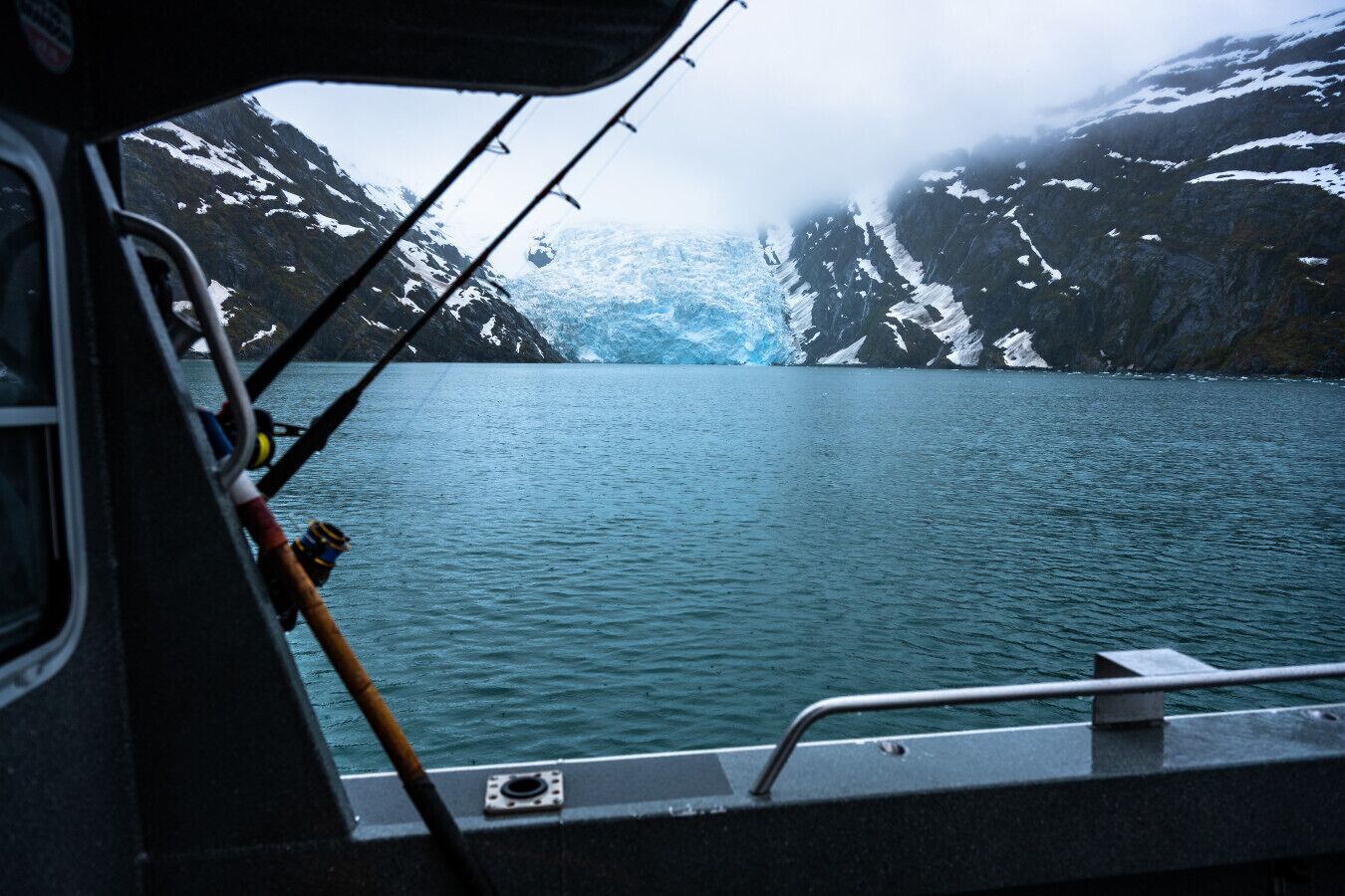 A boat's interior with fishing rods and a view of a glacier in the distance.