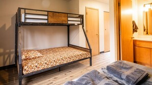 Uma cama beliche com estrutura de madeira e colchão estampado, cobertor cinza e uma porta de madeira ao fundo.