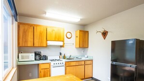 Uma cozinha compacta com armários de madeira, geladeira de aço inoxidável, micro-ondas, fogão e uma mesa de madeira com bancos.