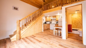 Eine Holztreppe führt zu einer Küche mit Holzboden, einem Essbereich und einem Badezimmer mit einer Badewanne.