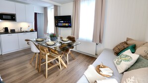 A modern kitchen with white cabinets, a microwave, and a dining area with a glass table and wooden chairs. - ALP APARTMENTS with self check-in (Engelberg)