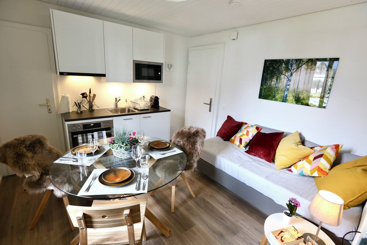 A modern kitchen with white cabinets, a microwave, and a dining area with a glass table and wooden chairs.