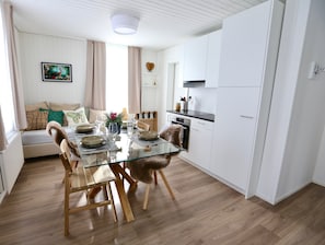 A modern kitchen with white cabinets, a glass dining table, and a wooden floor.