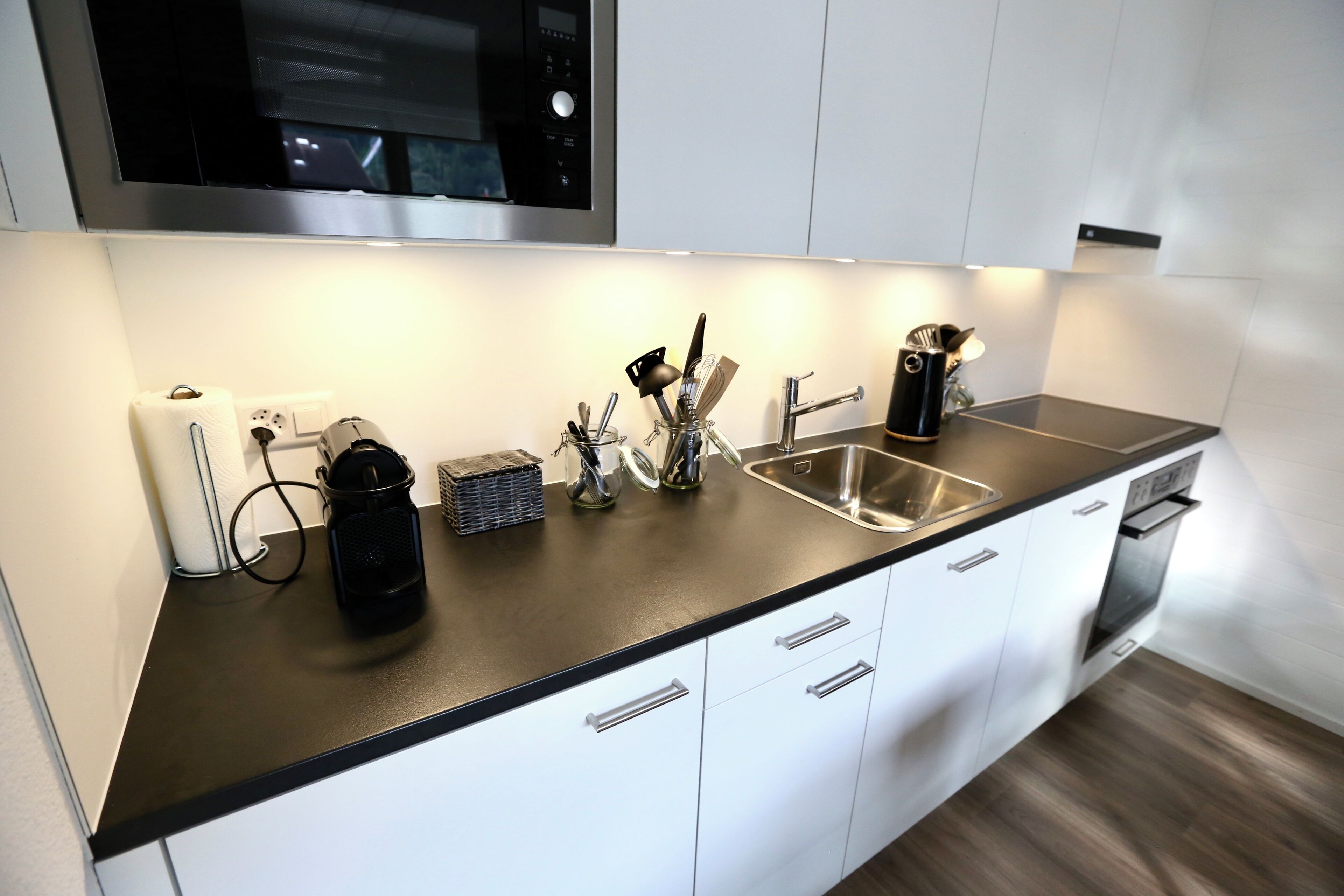 A modern kitchen with a stainless steel sink, white cabinets, and a black countertop.