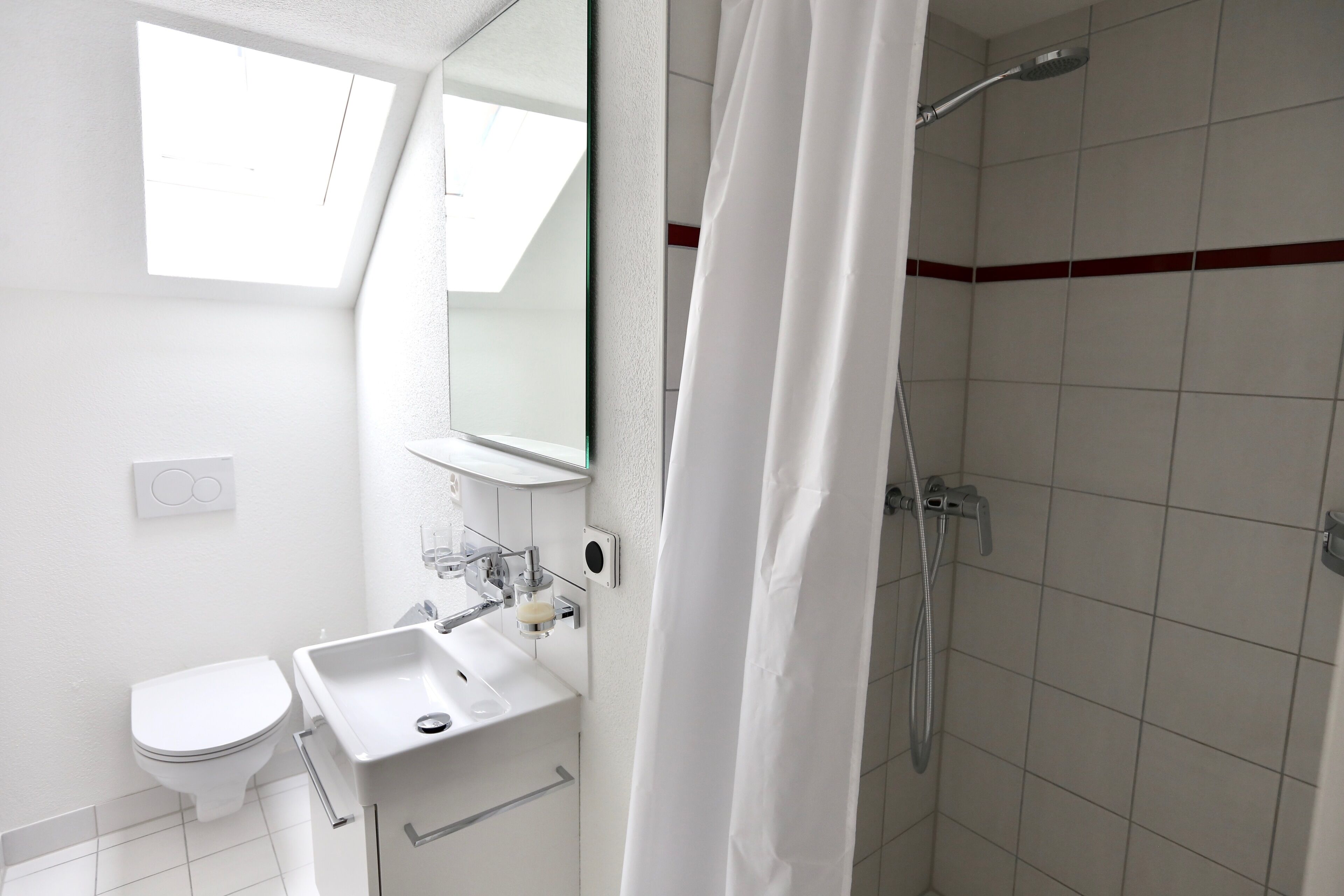 A bathroom with a toilet, sink, mirror, shower, and a skylight.