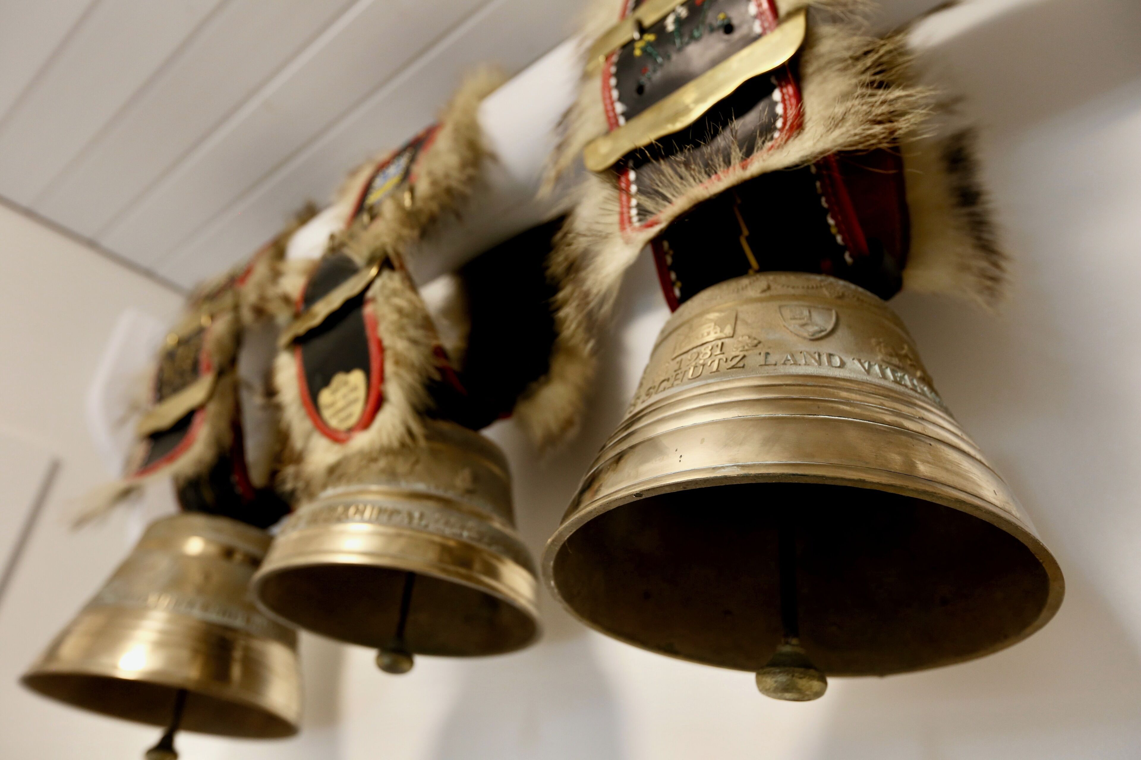 Une rangée de grandes cloches métalliques, ornées d’inscriptions, suspendues au plafond.