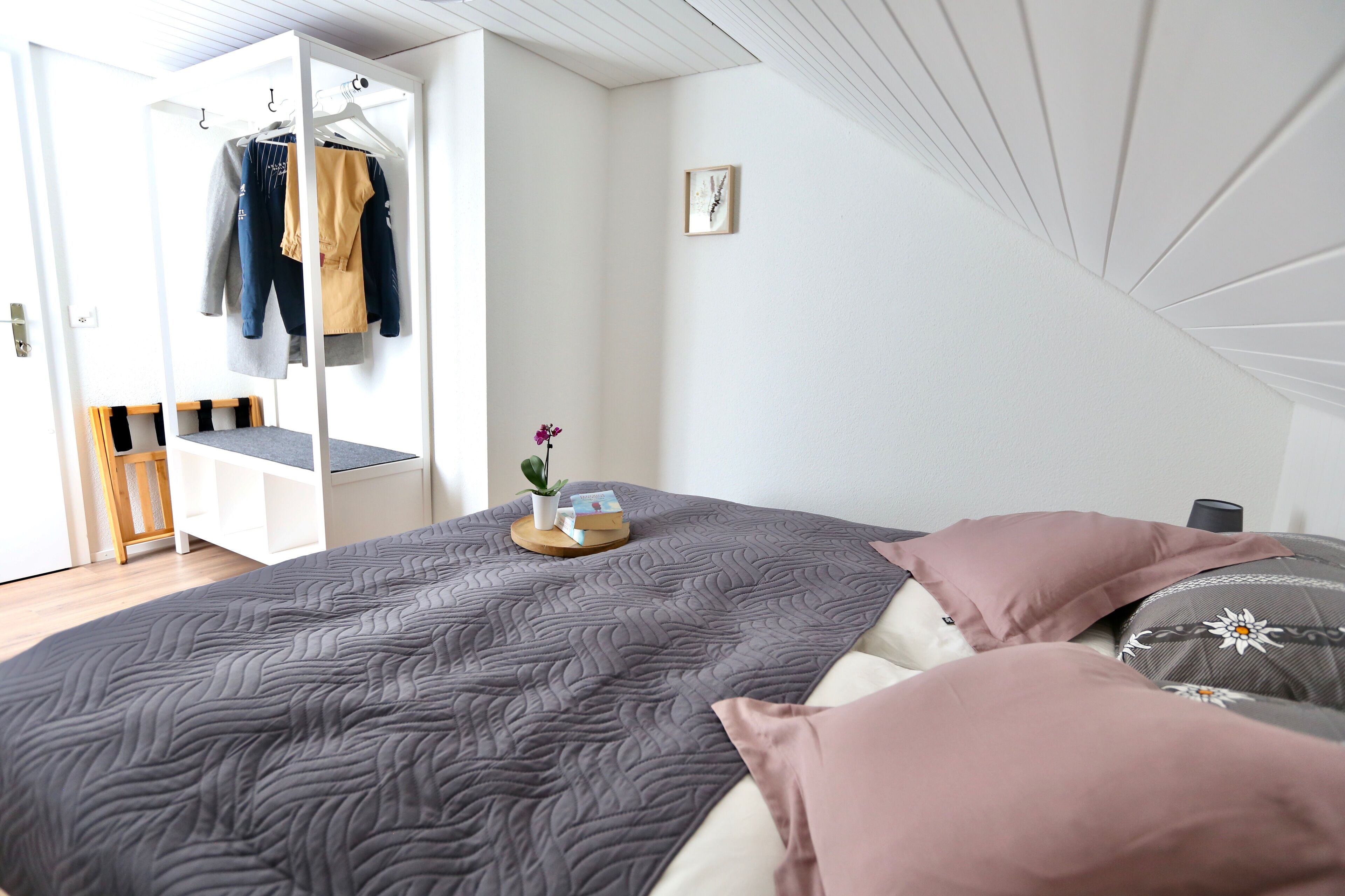 Un dormitorio con cama, armario y una mesita con una planta.
