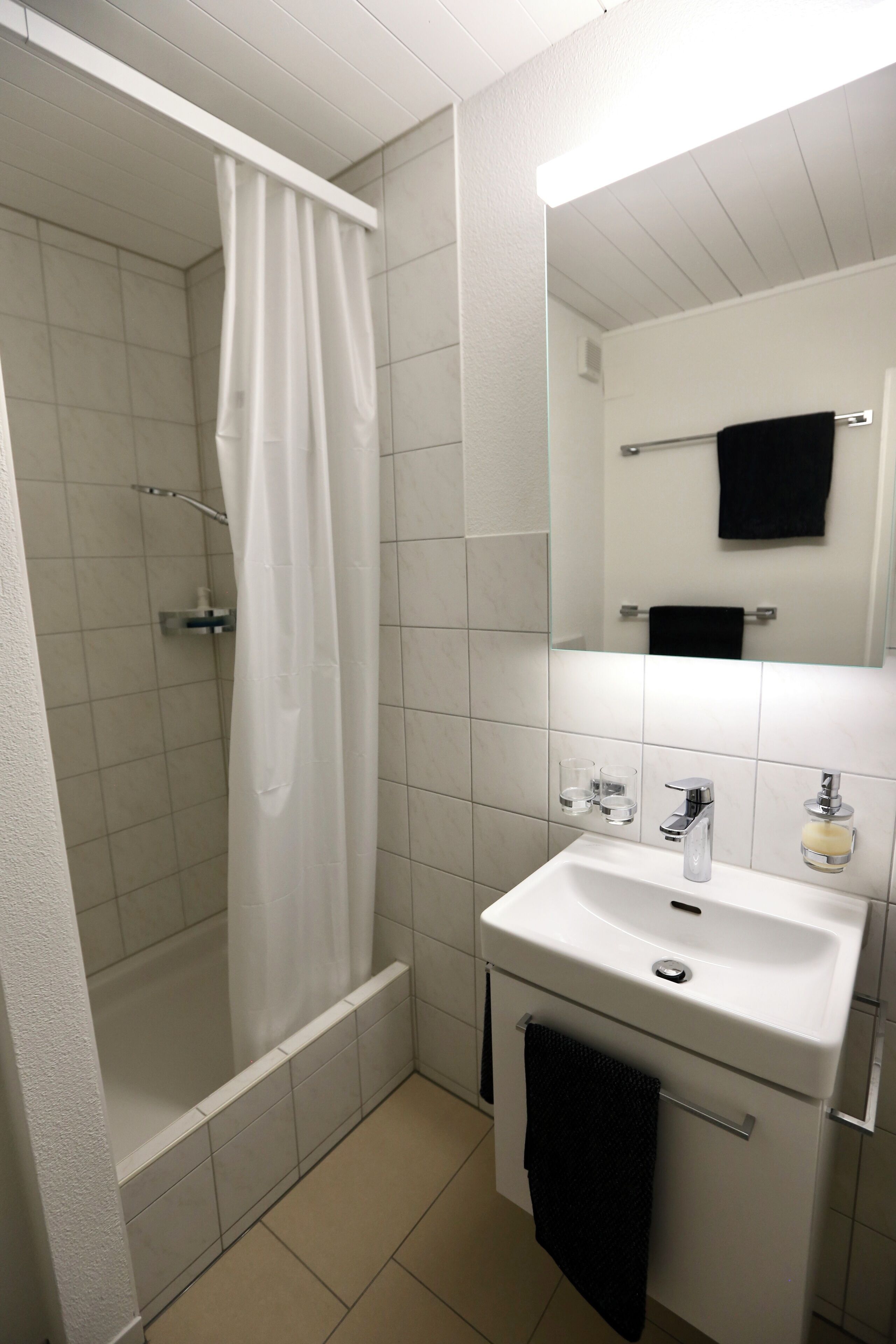 Ein Badezimmer mit Dusche, Waschbecken, Spiegel und Handtuchhalter.