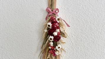 Une plaque en bois ornée d’un ruban rouge et blanc, décorée de fleurs séchées et de verdure.