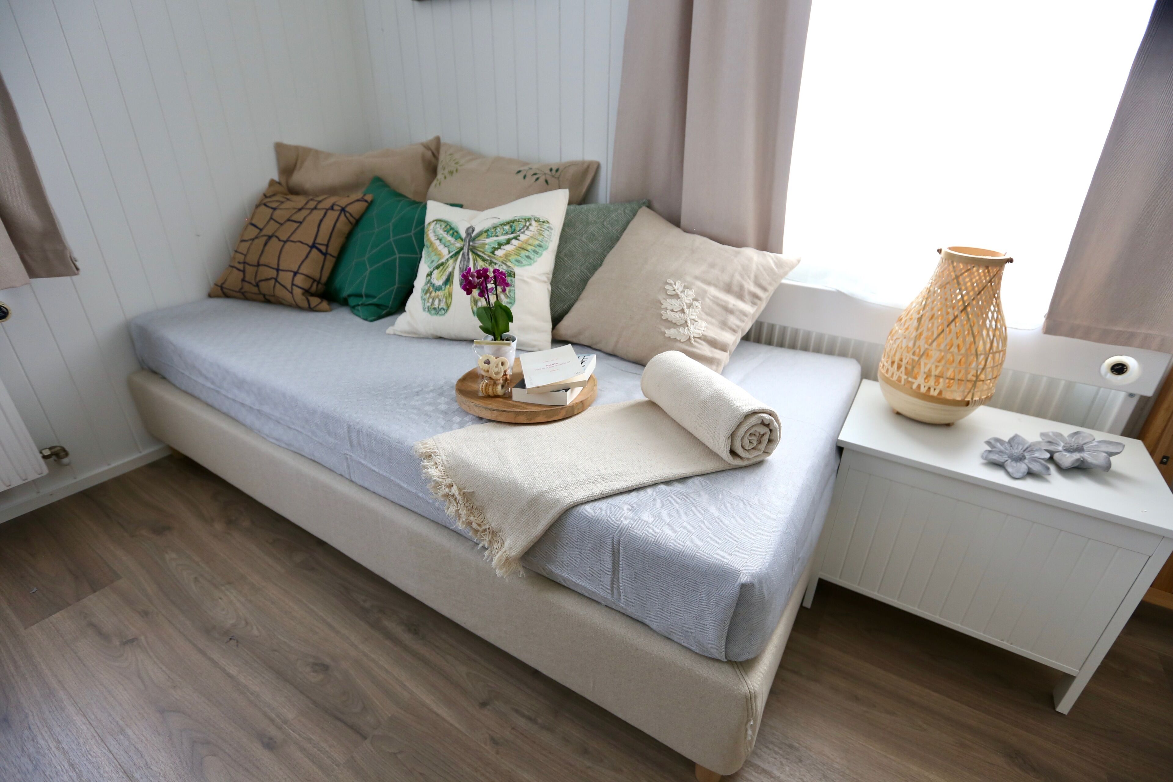 Une chambre à coucher bien rangée, avec un lit, des oreillers, une table de chevet avec une lampe et une fenêtre avec des rideaux.