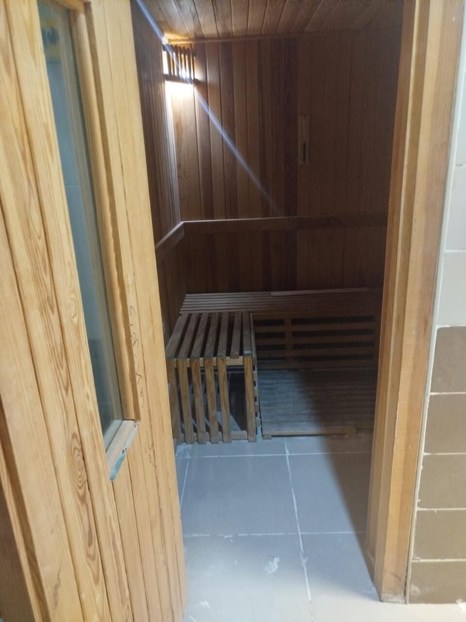 Un sauna en bois, avec des bancs, un plancher à lattes et un mur carrelé.