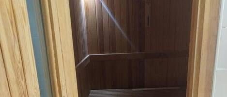 A wooden sauna room with benches, a slatted floor, and a tiled wall.