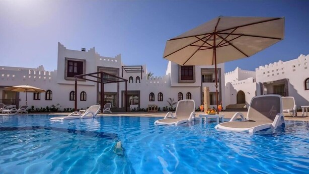 A swimming pool with lounge chairs and umbrellas, surrounded by white buildings with arched windows and balconies. - Mazar Resort & Spa By Kemet (Sharm El Sheikh)