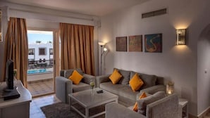A modern living room with a grey sofa set, a coffee table, and a TV on a stand. There are two floor lamps and artwork on the wall. - Mazar Resort & Spa By Kemet (Sharm El Sheikh)