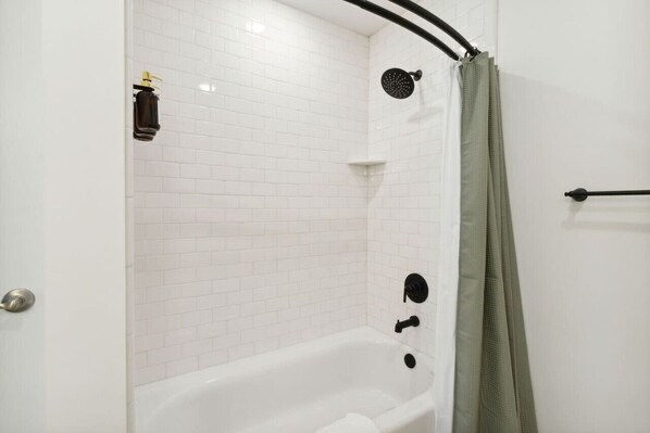 Une cabine de douche aux parois recouvertes de carreaux blancs, dotée d’un pommeau de douche noir, d’un pommeau de douche à main et d’un robinet à main.