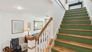 Eine Treppe mit Holzdielen und einem grünen Teppich, die zu einer Zwischenebene mit einer Lampe und gerahmten Bildern führt.