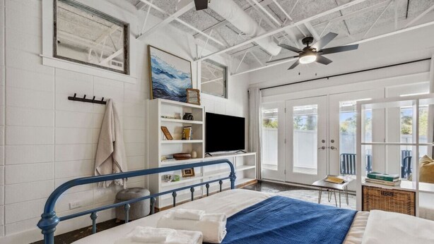 A bedroom with a bed, a TV, a ceiling fan, and a window.