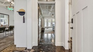 A hallway with white walls, a black floor, and a ceiling with exposed beams. There is a door on the right and a window on the left.