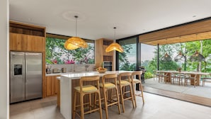 Une cuisine moderne dotée d’un grand îlot central, de chaises en bois et de luminaires suspendus.