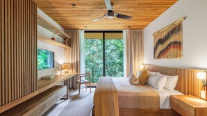 Une chambre moderne avec un plafond en bois, un lit recouvert de draps blancs, un bureau avec une télévision et une grande fenêtre donnant sur des arbres.