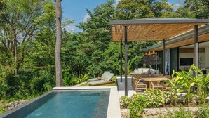 Un espace piscine extérieur moderne, doté d’une terrasse en bois, de chaises longues et d’un coin salon abrité.