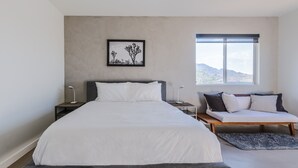 Un dormitorio moderno con una cama grande, mesitas de noche, un banco y una ventana con vistas.