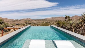 Una piscina rectangular con agua cristalina azul, rodeada de vegetación desértica y montañas al fondo.