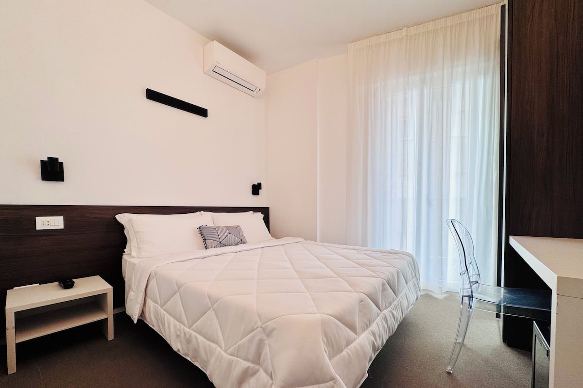 A hotel room with a bed, bedside table, and a desk with a chair.