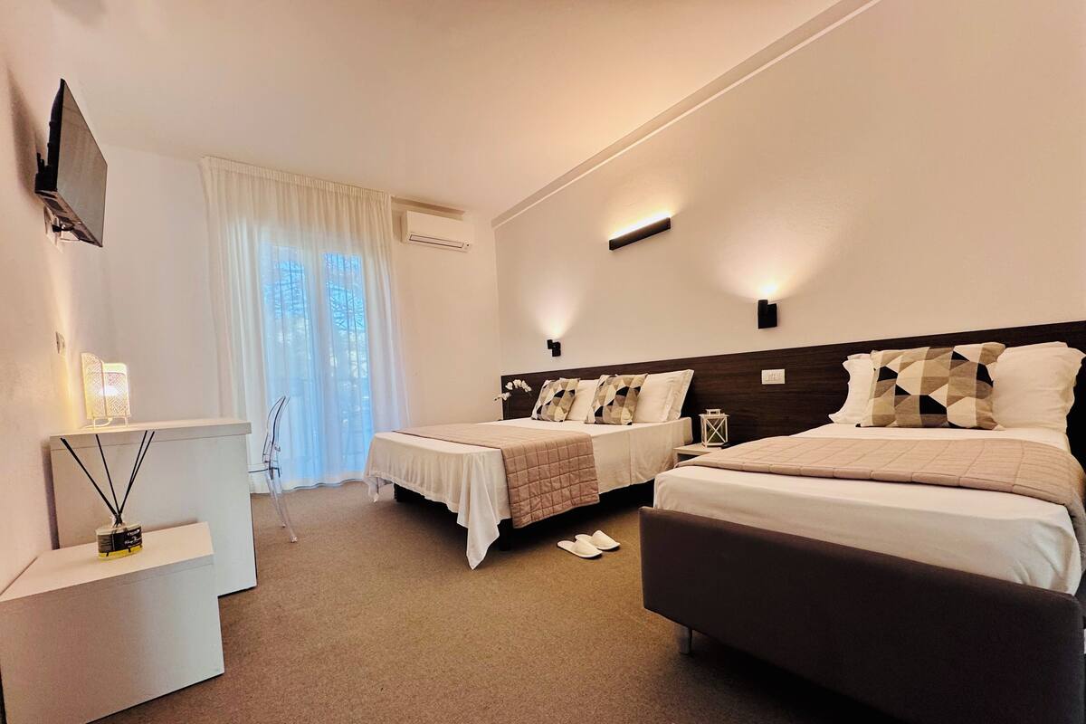 A hotel room with two beds, a desk, a TV, and a window with curtains.