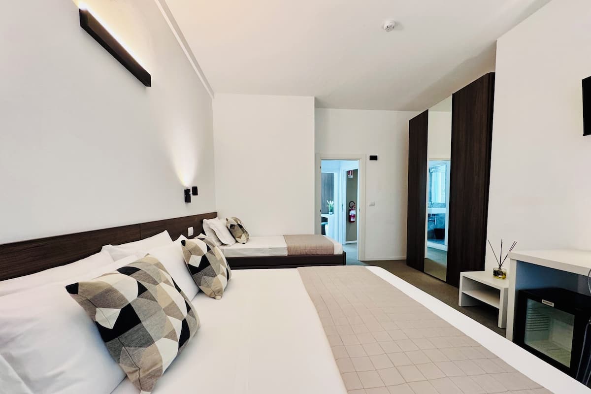 A modern hotel room with a large bed, a bedside table, a TV, and a view of the outside.