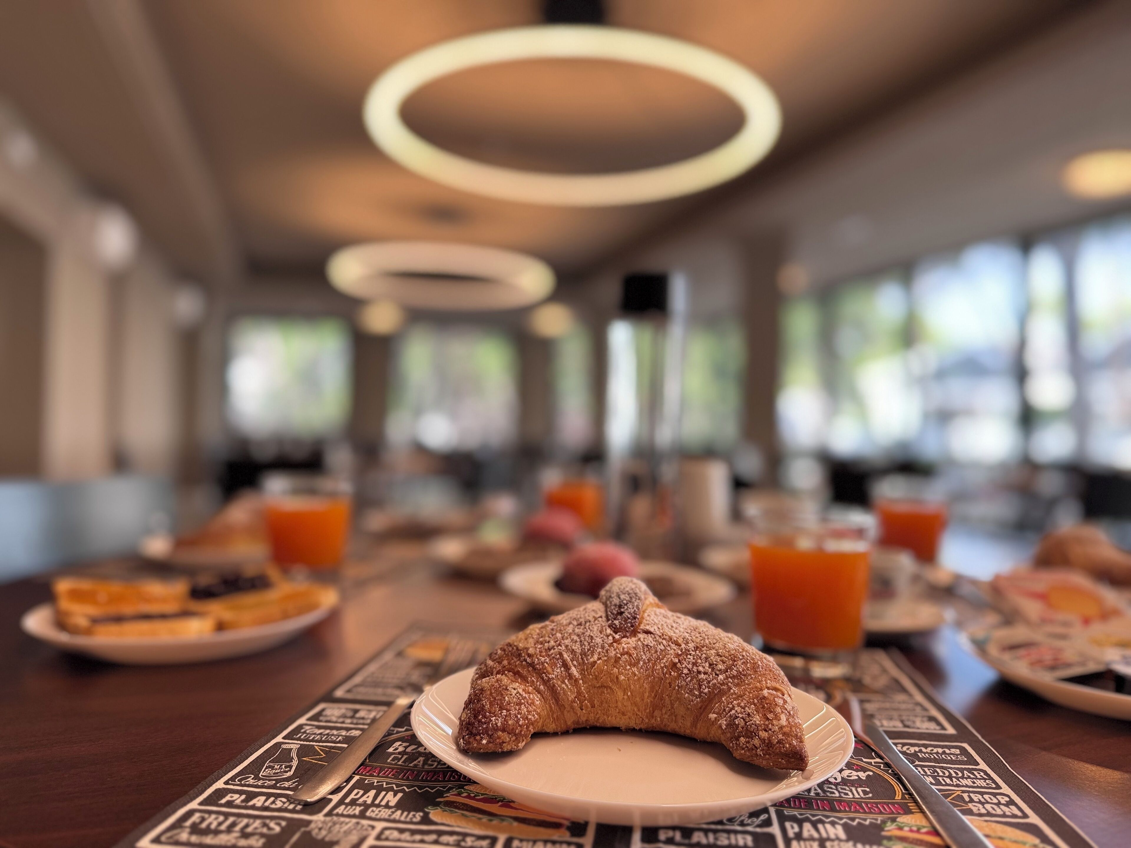 Un desayuno con un croissant en un plato, zumo de naranja y otros productos para el desayuno sobre una mesa.