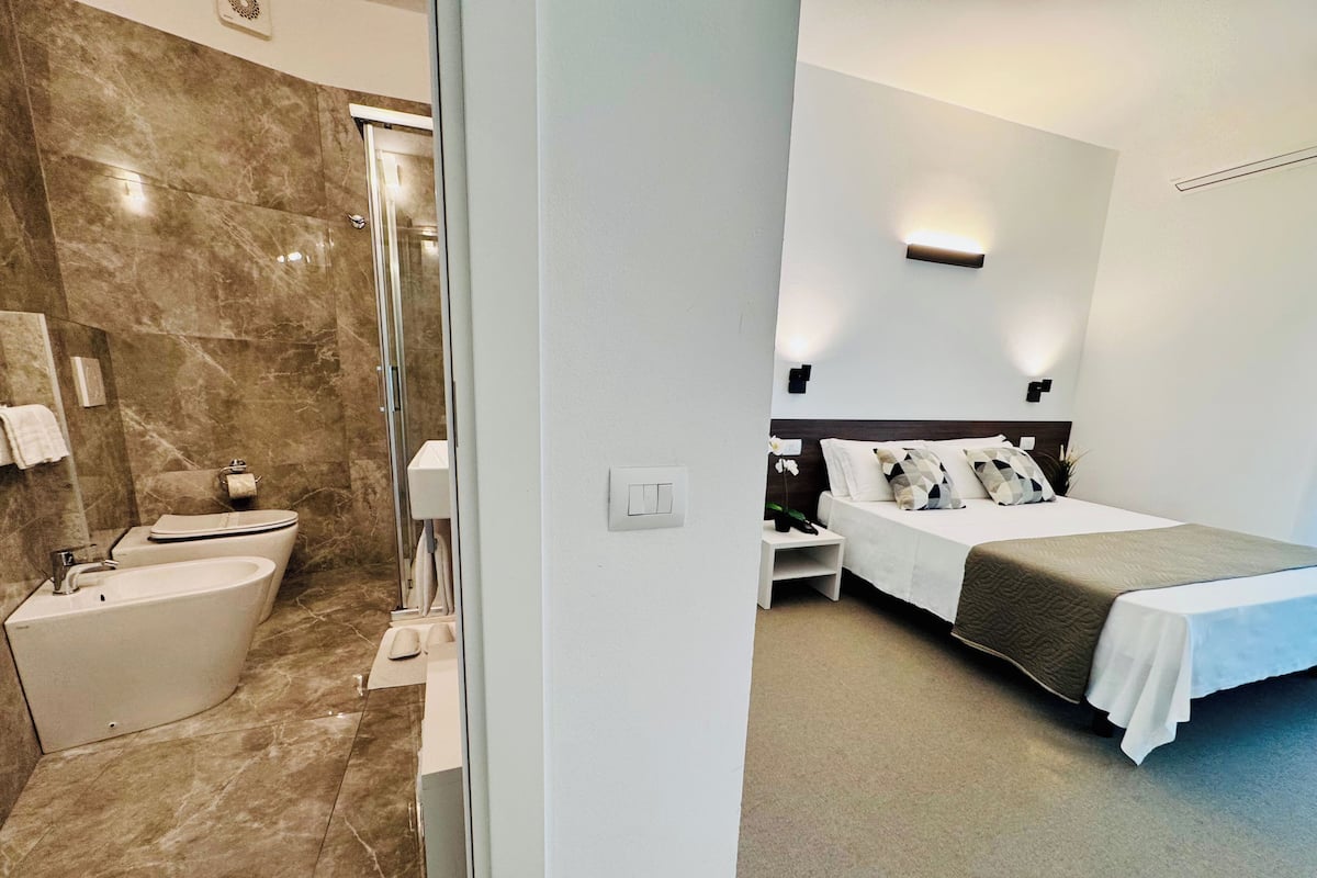 A modern hotel room with a bathroom, a bed, and a nightstand.