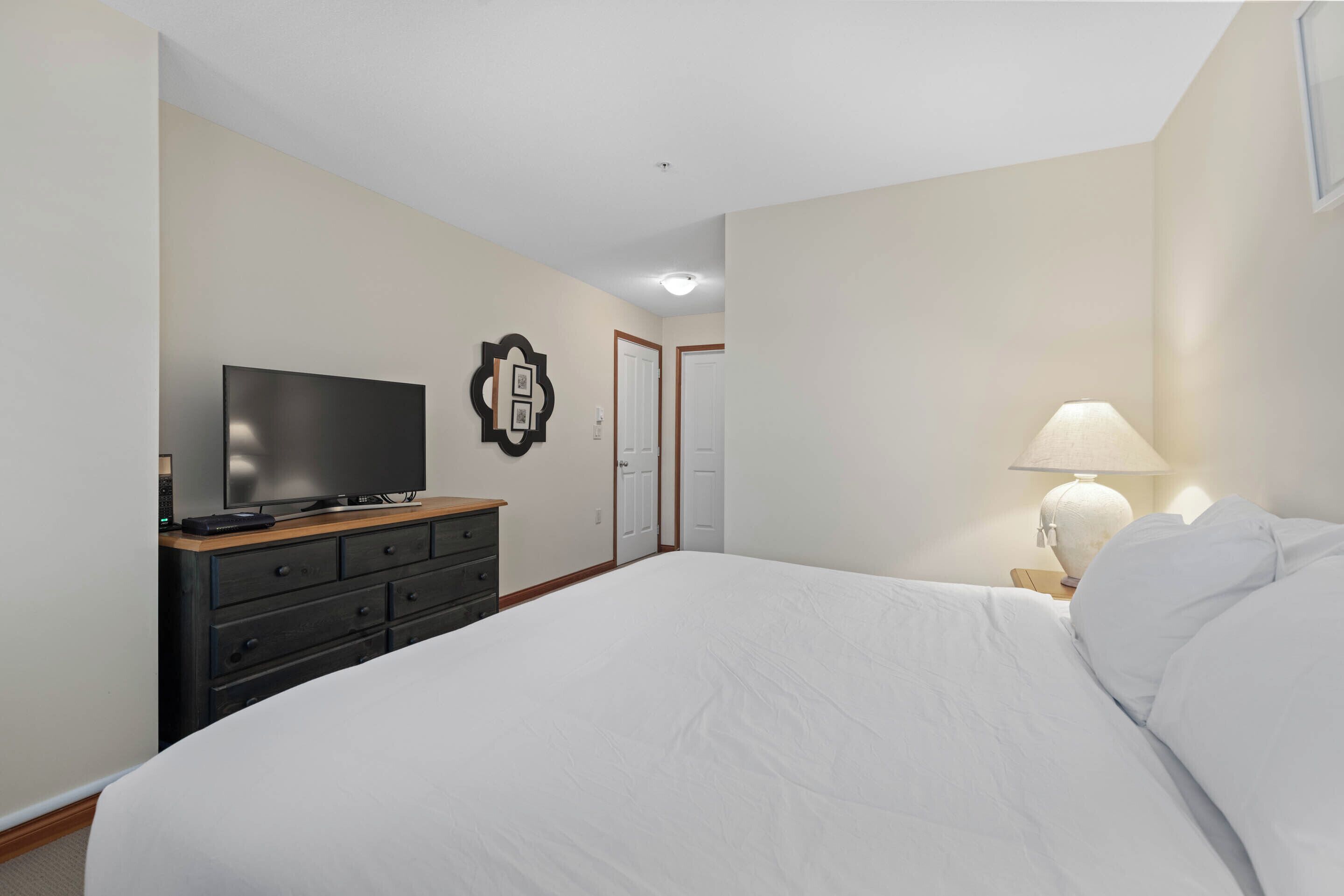 A hotel room with a bed, a TV on a dresser, a lamp, and a door.