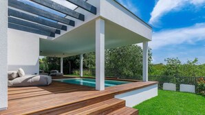Un espace piscine extérieur moderne, doté d’une terrasse en bois et d’un coin salon abrité.