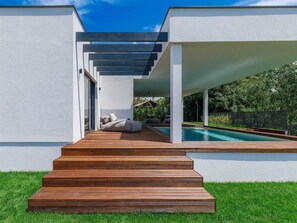 Un espace piscine extérieur moderne, agrémenté d’un escalier en bois menant à un espace détente abrité.