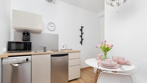 Une cuisine moderne équipée d’un four à micro-ondes, d’une machine à café et d’un lave-vaisselle. On y trouve une table à manger avec des assiettes et des verres roses.