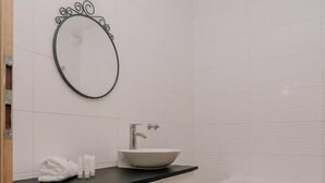 Une salle de bain moderne avec un meuble-lavabo blanc, un miroir rond, un lavabo et une baignoire.