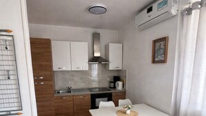 A compact kitchen with white cabinets, a dining table with chairs, a kitchen island, and a built-in oven. - Seafront Paradise at Rab Island - Emily 3 (Kampor)