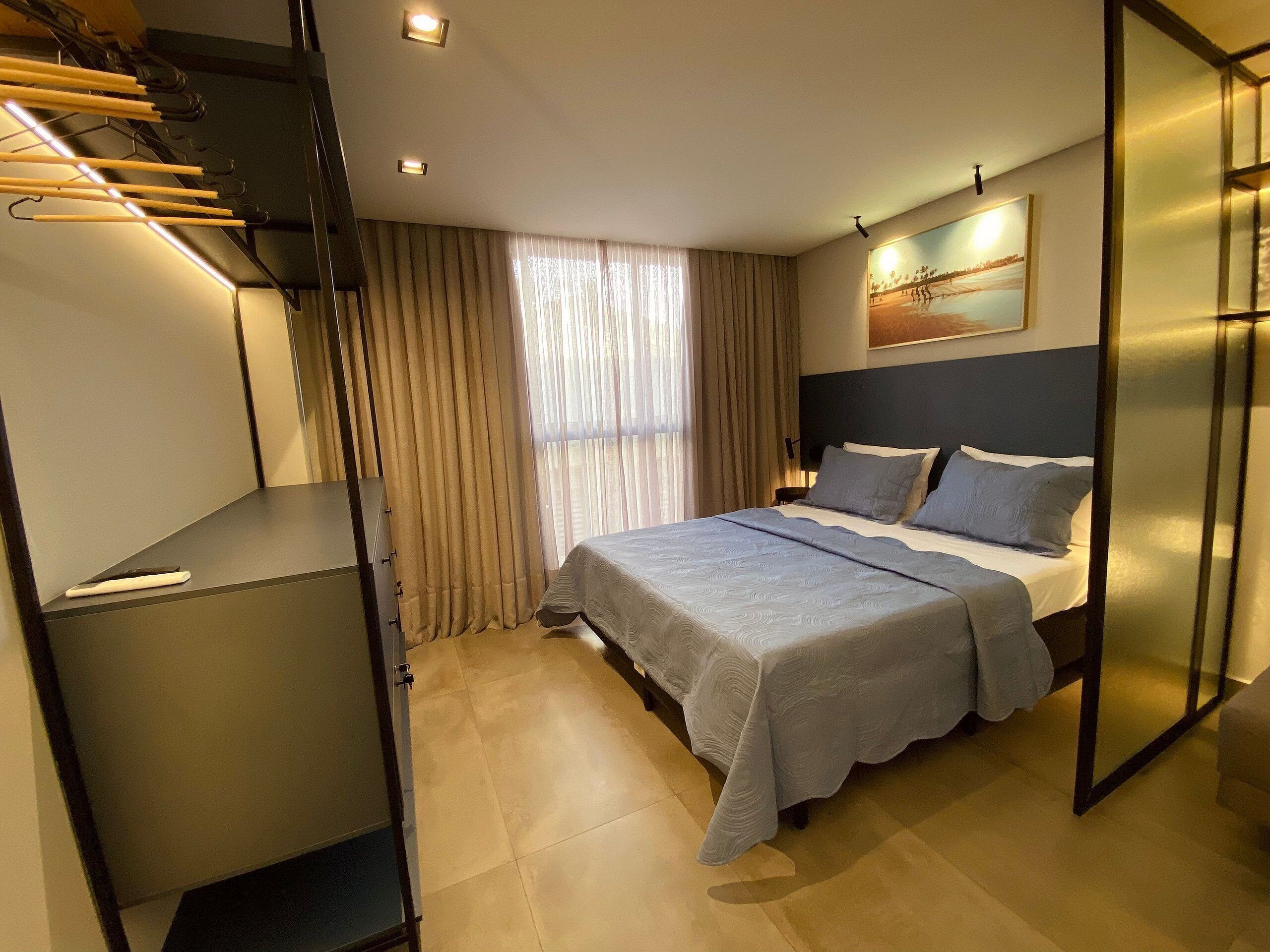A modern hotel room with a bed, a desk, and a wardrobe.