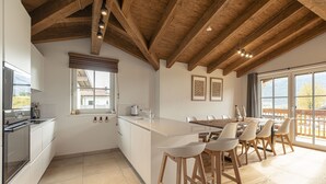 A modern kitchen with wooden beams, a large island, bar stools, and a dining area with a view. - Superior Ferienhaus # 3B mit Sauna (Uttendorf)