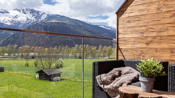 A balcony with a view of a mountain range, a wooden cabin, and a grassy field. - Superior Ferienhaus # 3B mit Sauna (Uttendorf)