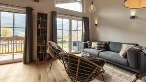A spacious living room with a grey sofa, wicker chairs, and a glass cabinet. Large windows offer a view of the outdoors. - Superior Ferienhaus # 3B mit Sauna (Uttendorf)