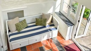 Et hyggeligt rum med hvide vægge, et vindue med udsigt, en hvid sofa med puder og en hængende lampe.