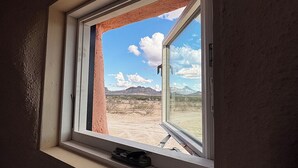 Una ventana con vistas a un paisaje desértico, incluyendo montañas y vegetación escasa.