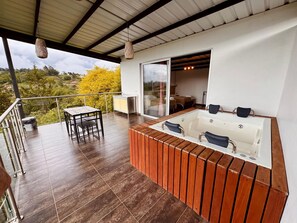 A balcony with a wooden table and chairs, a hot tub, and a glass door leading to a bedroom. - CABINS WITH BEAUTIFUL VIEWS, WITH JACUZZI GUATAPE (Antioquia)
