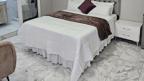 A bedroom with a large bed, a nightstand, a chair, and a bathroom visible through an open door.